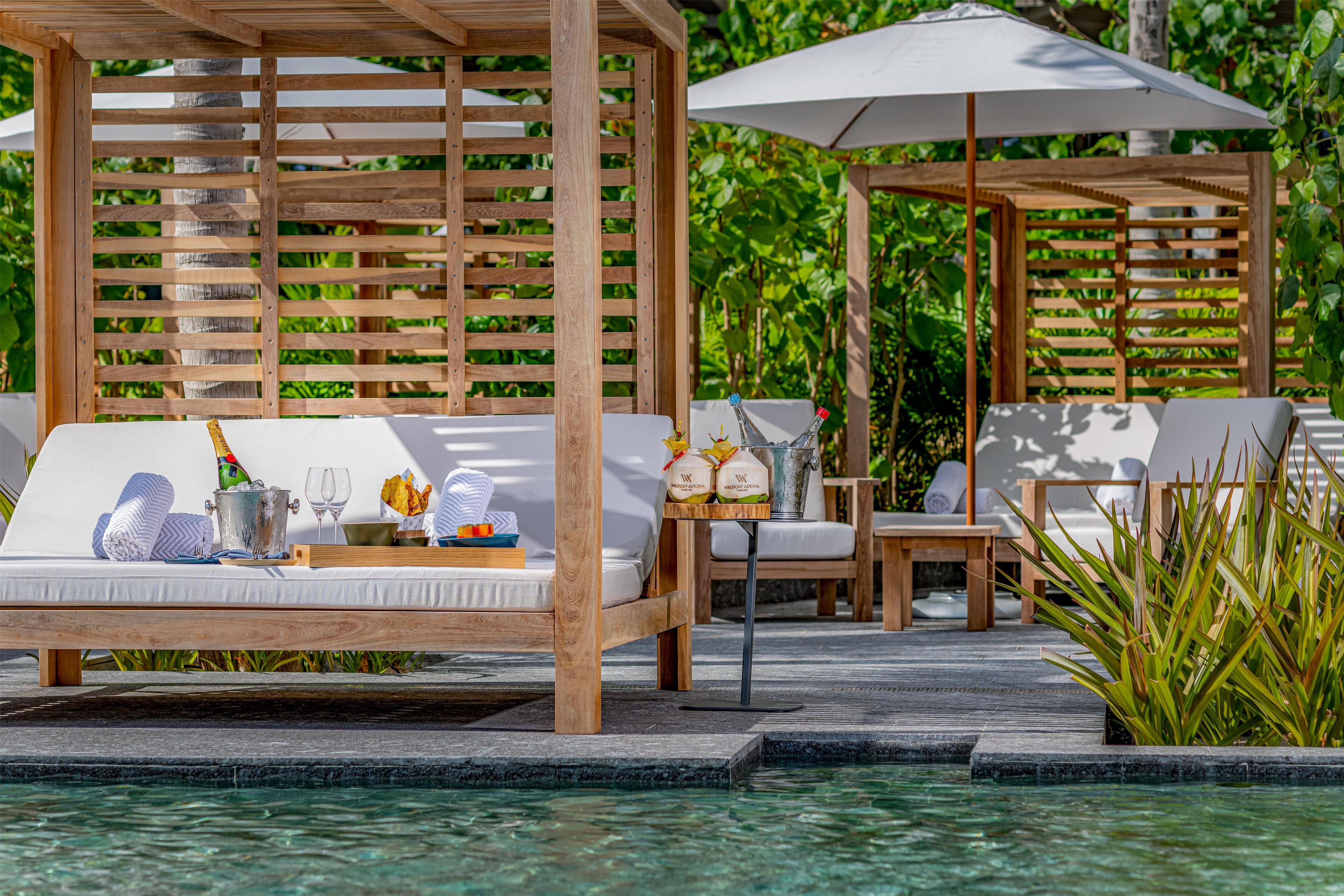 Un espace de détente aménagé au bord de la piscine, avec des pergolas en bois, des chaises longues et une table équipée de tout le nécessaire.