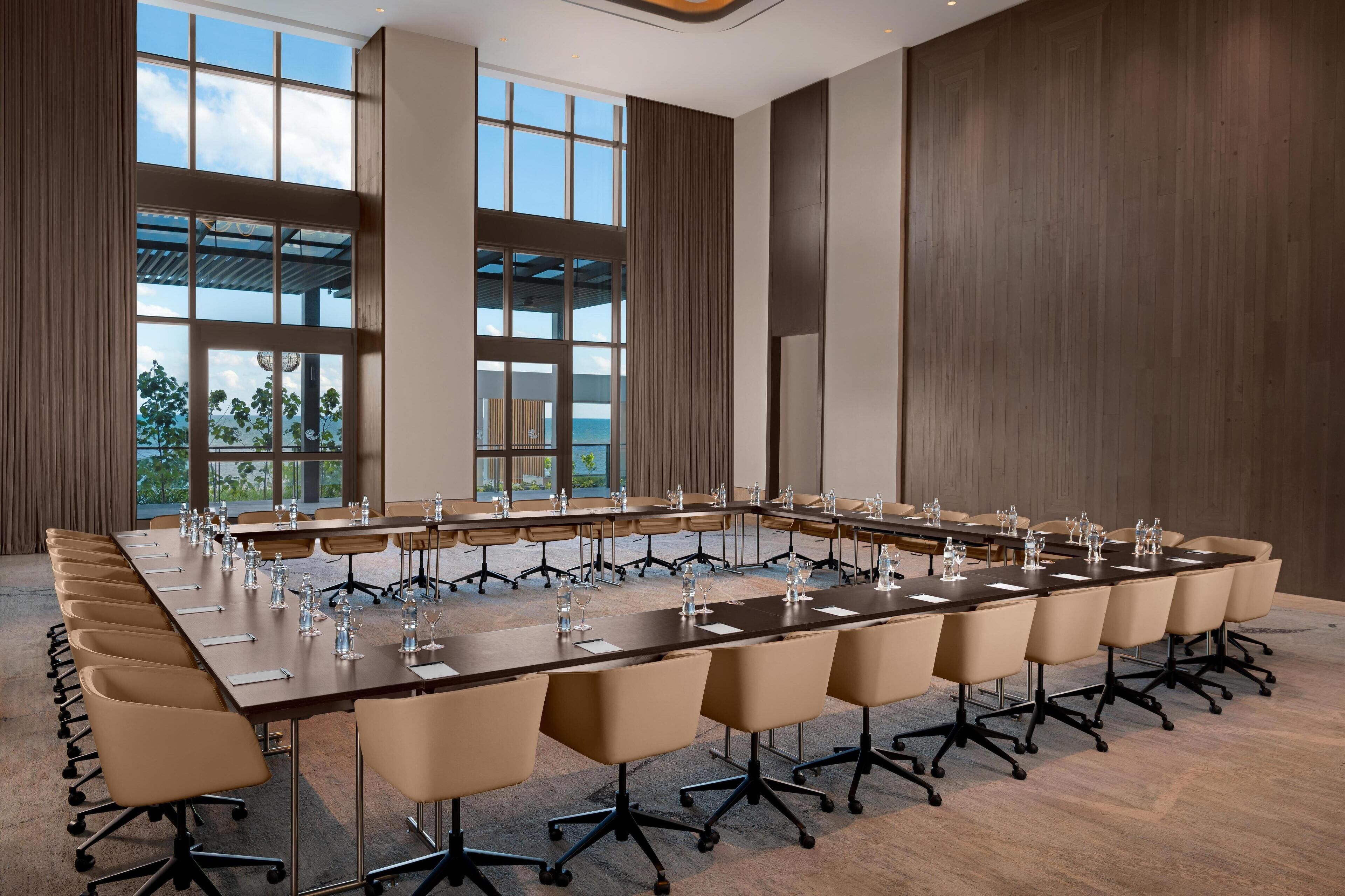 A conference room with a long table, multiple chairs, and large windows offering a view of the outdoors.