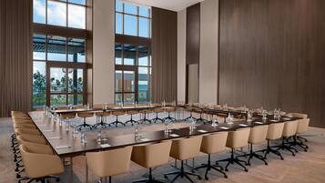 A conference room with a long table, multiple chairs, and large windows offering a view of the outdoors.