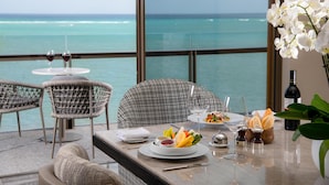 A dining table with a view of the ocean, wicker chairs, and a bottle of wine. - Waldorf Astoria Riviera Maya (Cancun)