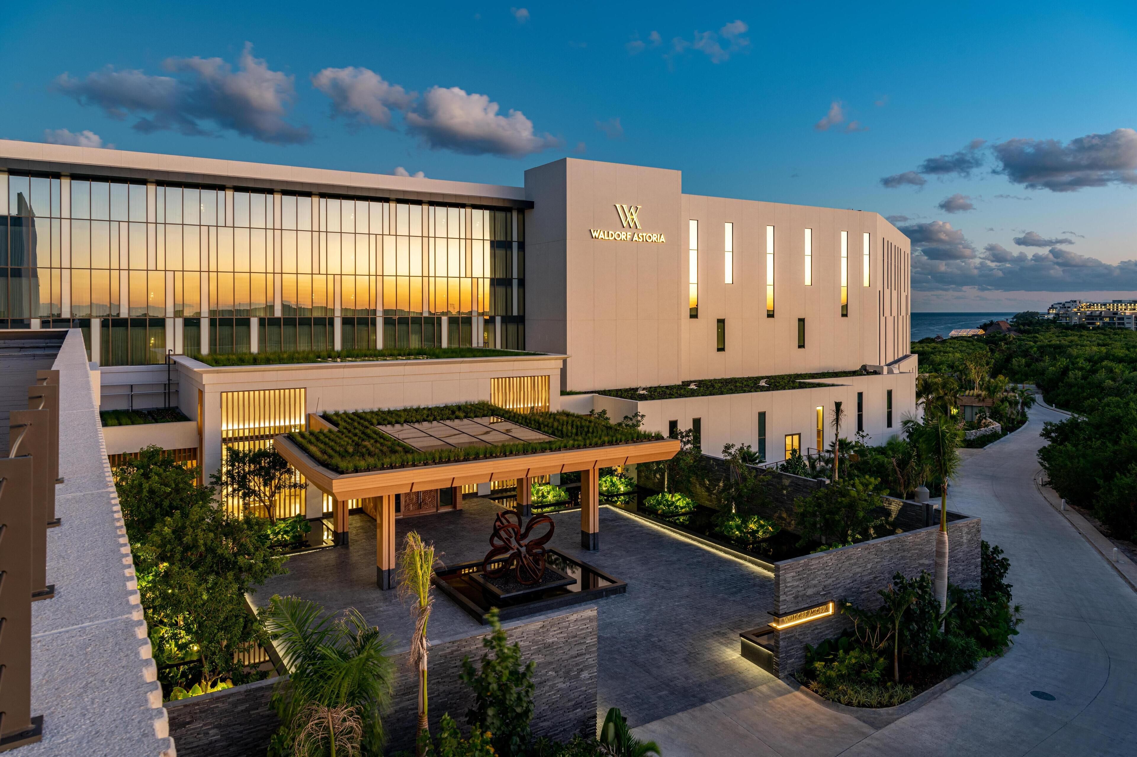 A modern hotel with a large glass facade, a rooftop garden, and a well-maintained outdoor area with pathways and greenery.