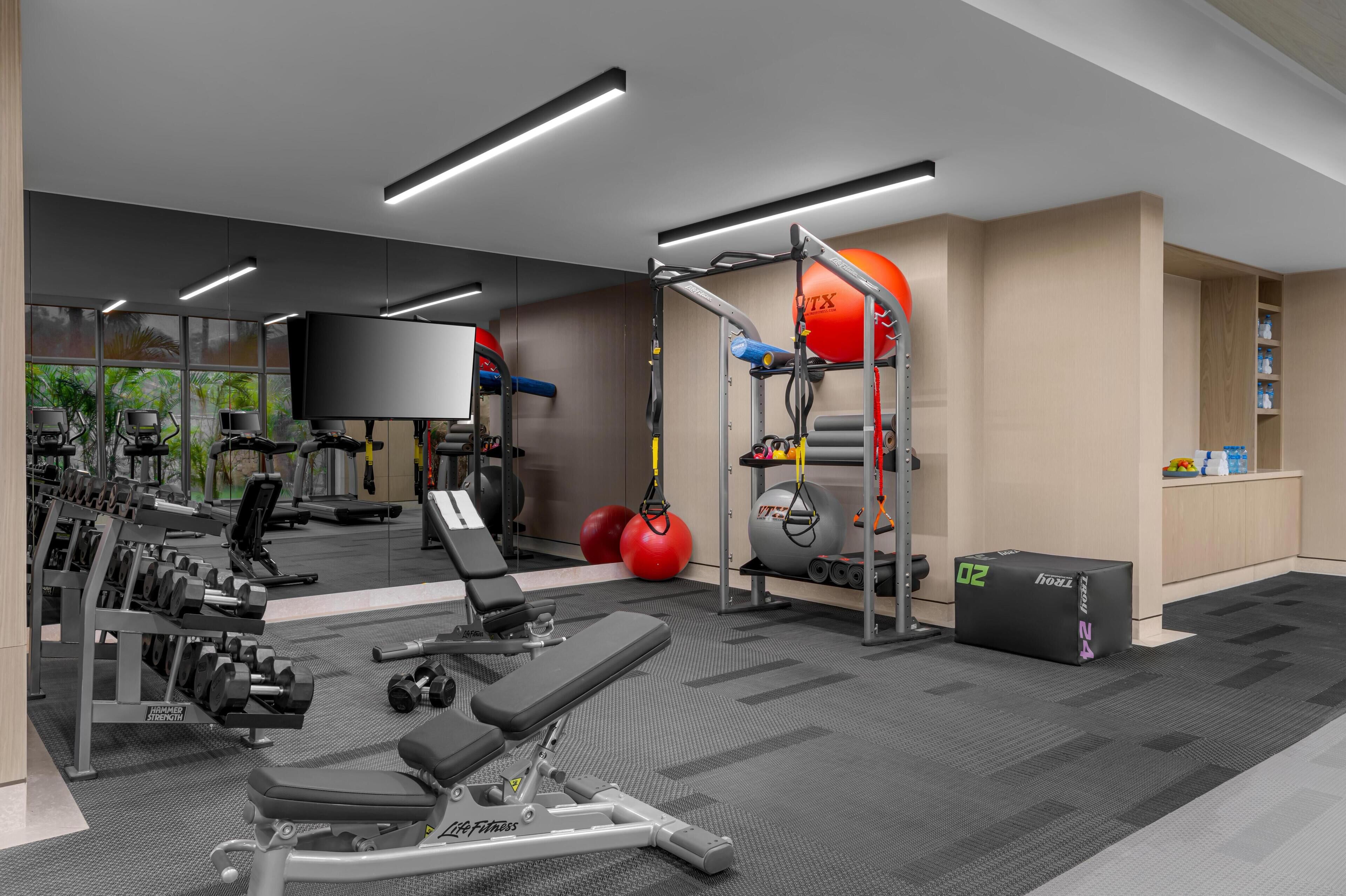 A modern gym with exercise equipment, a TV, and a large window.