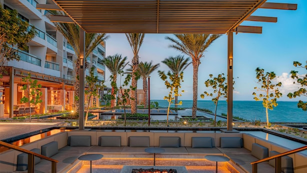 A modern outdoor seating area with a fire feature, palm trees, and a view of the ocean. - Waldorf Astoria Riviera Maya (Cancun)