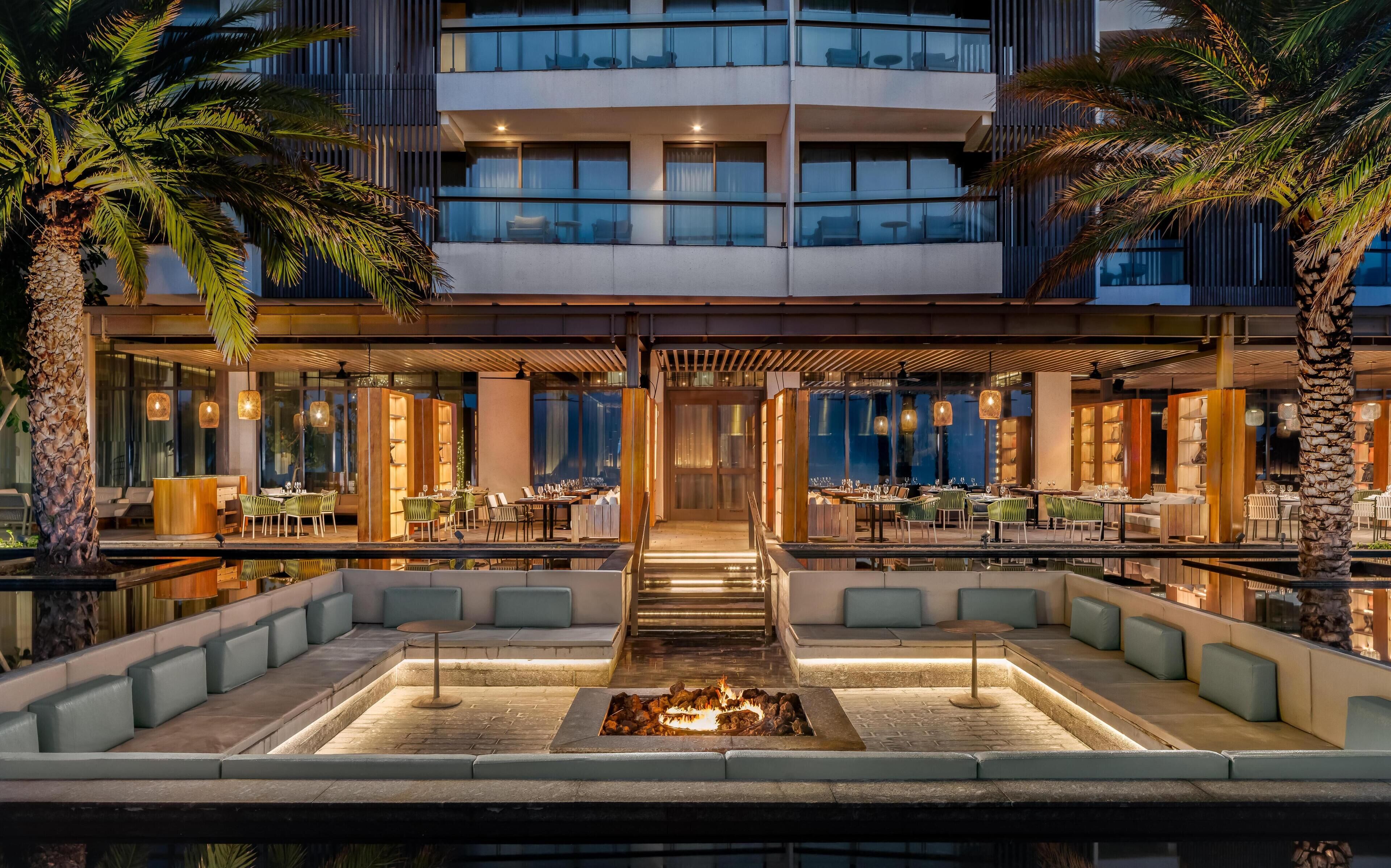 A modern hotel with a pool area, outdoor seating, and a fire feature.