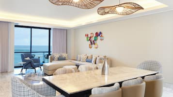 Ein modernes Wohnzimmer mit großem Esstisch, bequemen Sitzmöglichkeiten, einer dekorativen Wandgestaltung und Meerblick.