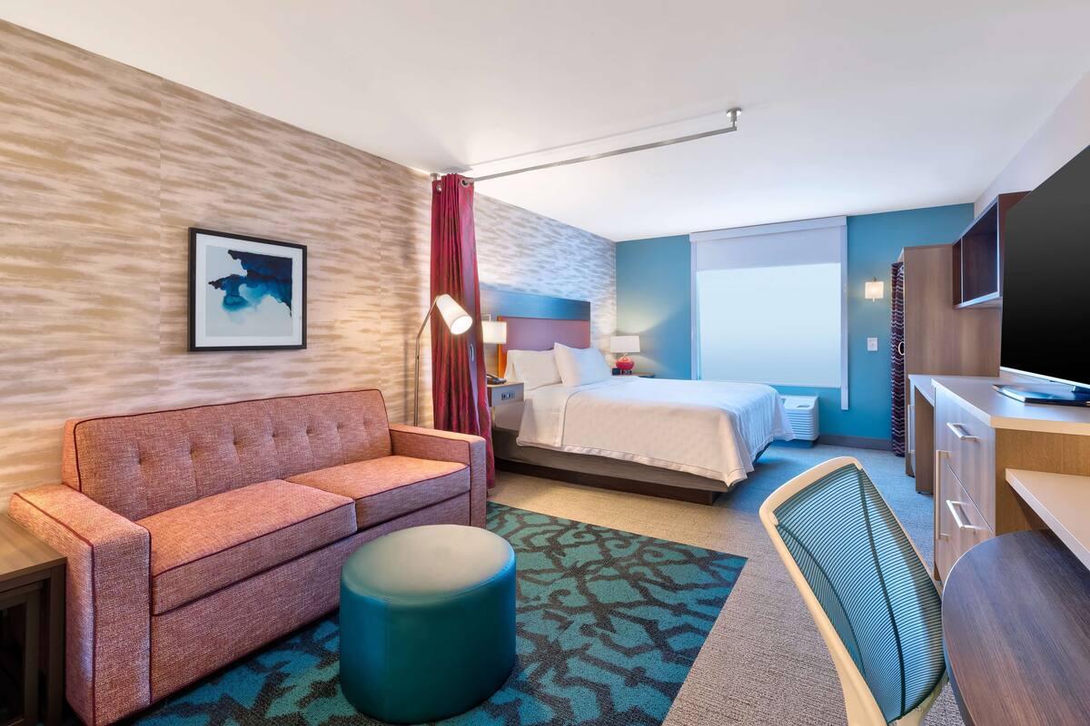 Ett hotellrum med en säng, en soffa, ett skrivbord, en stol och en tv.