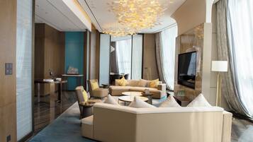A modern hotel room with a large sofa, armchairs, a coffee table, and a TV.