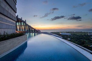 Un hotel moderno con una piscina larga, un puente de cristal y vistas a la ciudad al atardecer.