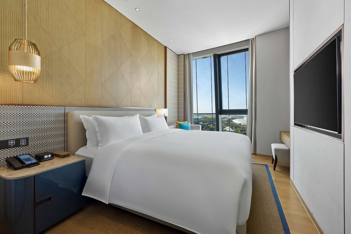 Una habitación de hotel moderna con una cama grande, un escritorio con teléfono y vistas a la ciudad a través de amplias ventanas.