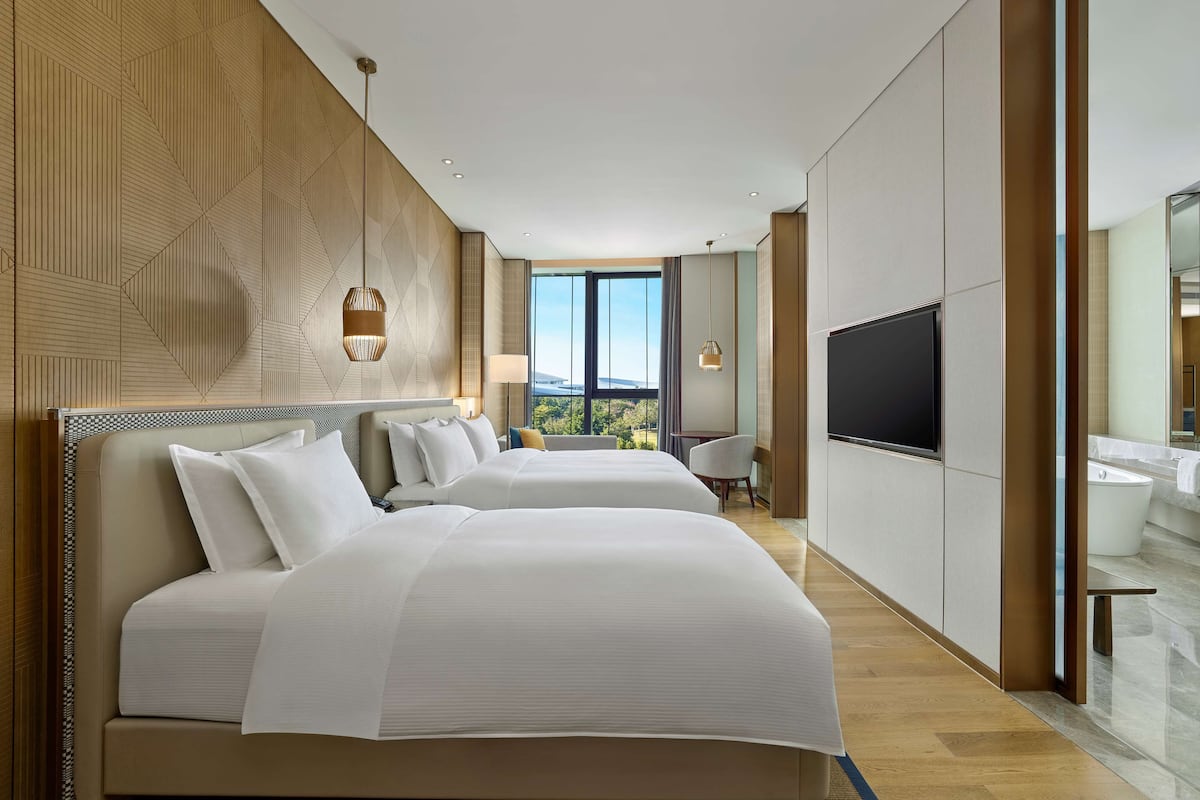 Habitación de hotel moderna con dos camas, un televisor grande y vistas al exterior.