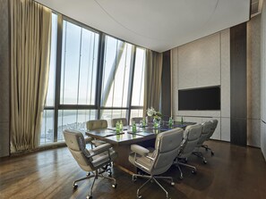 Un salón de conferencias con una gran mesa, cuatro sillas de oficina, un televisor de pantalla plana y vista a un cuerpo de agua a través de amplias ventanas.