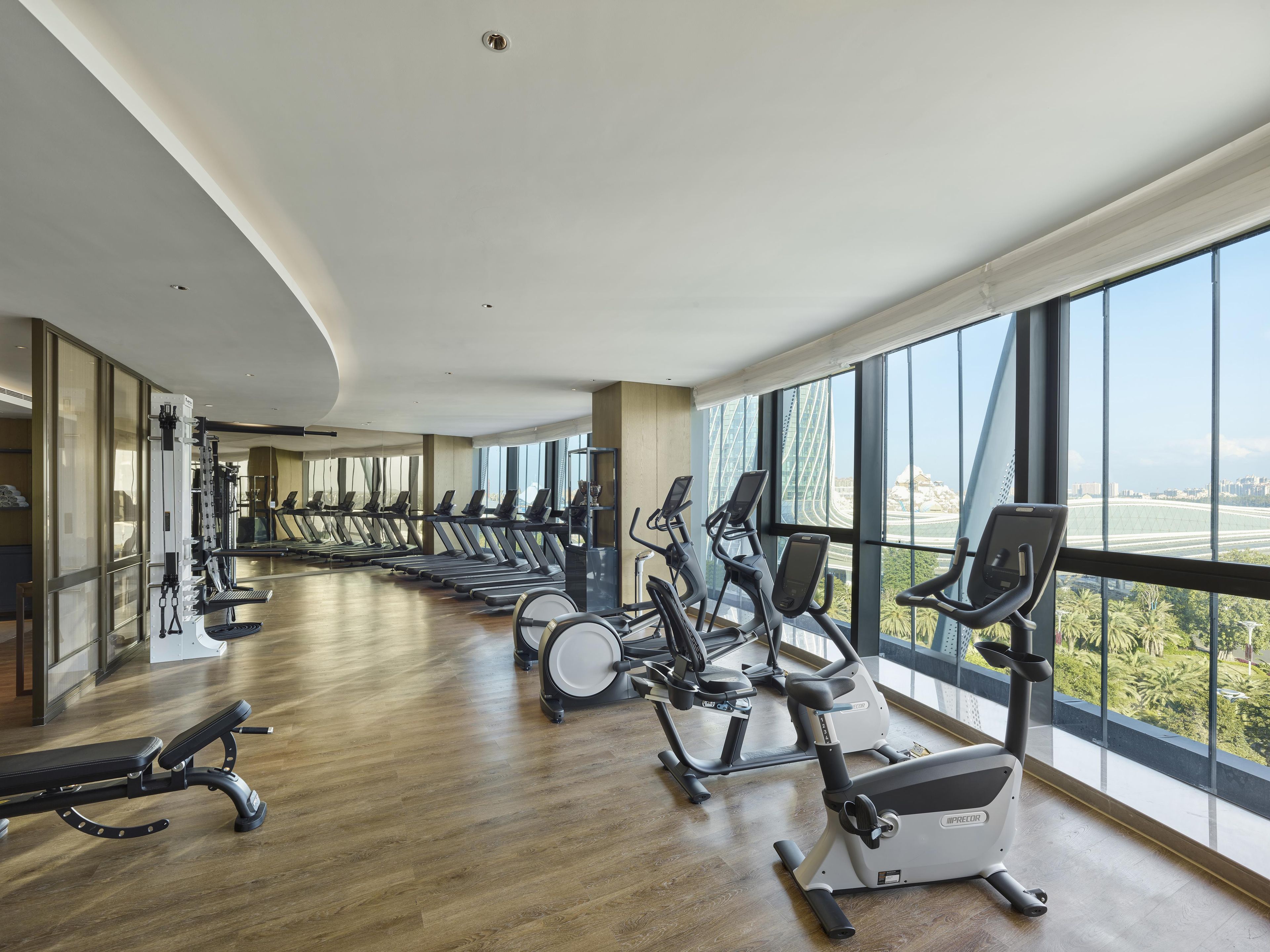 A gym with cardio machines and a bench, large windows, and a view of a bridge.
