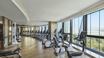 A gym with cardio machines and a bench, large windows, and a view of a bridge.