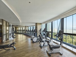 Un gimnasio con máquinas de cardio y una banca, ventanas amplias y vistas a un puente.