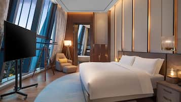 Habitación de hotel moderna con una cama grande, un televisor, un escritorio con lámpara y vistas a la ciudad a través de amplias ventanas.