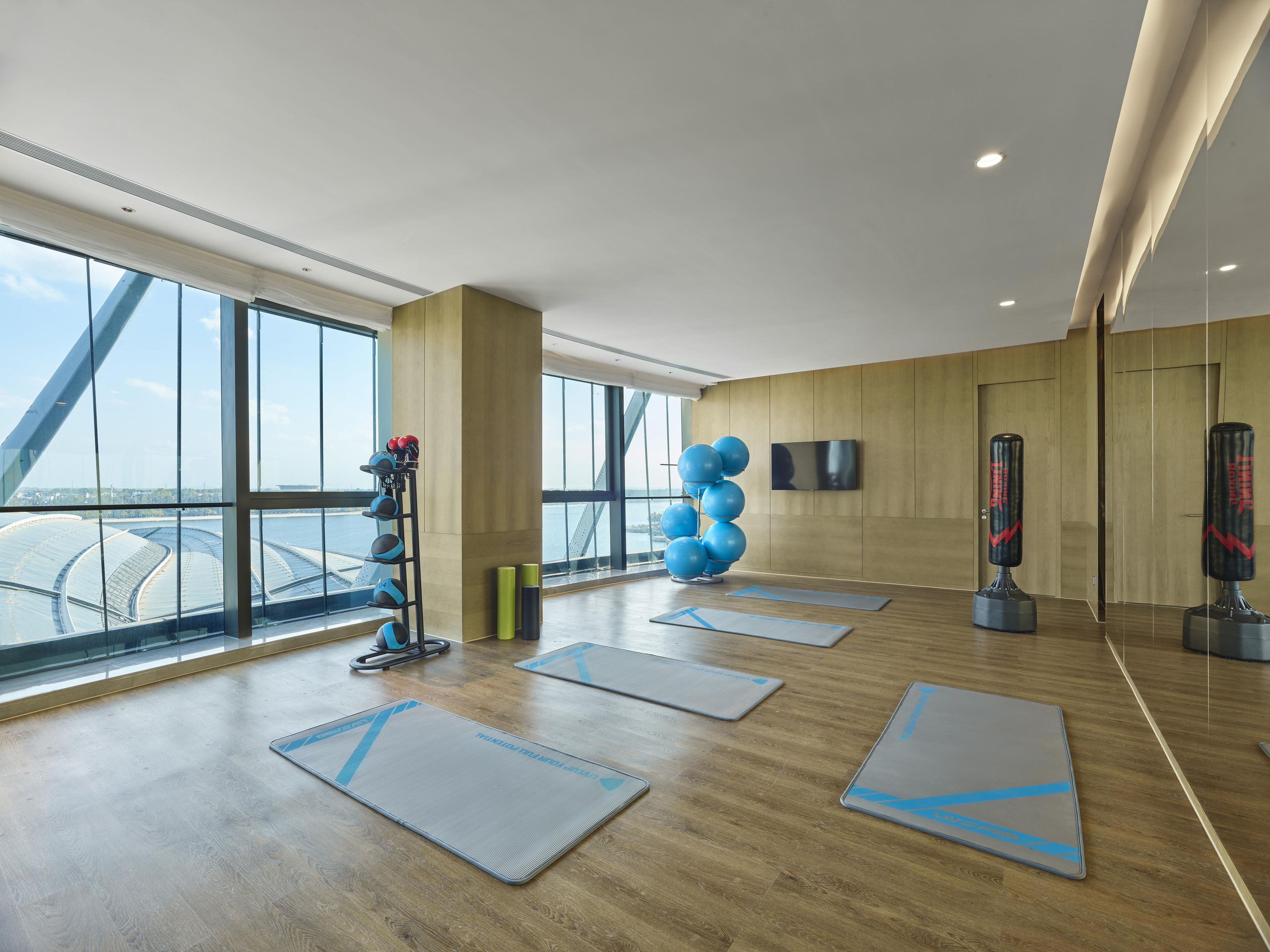 A spacious gym with exercise mats, a punching bag, and a wall-mounted TV.