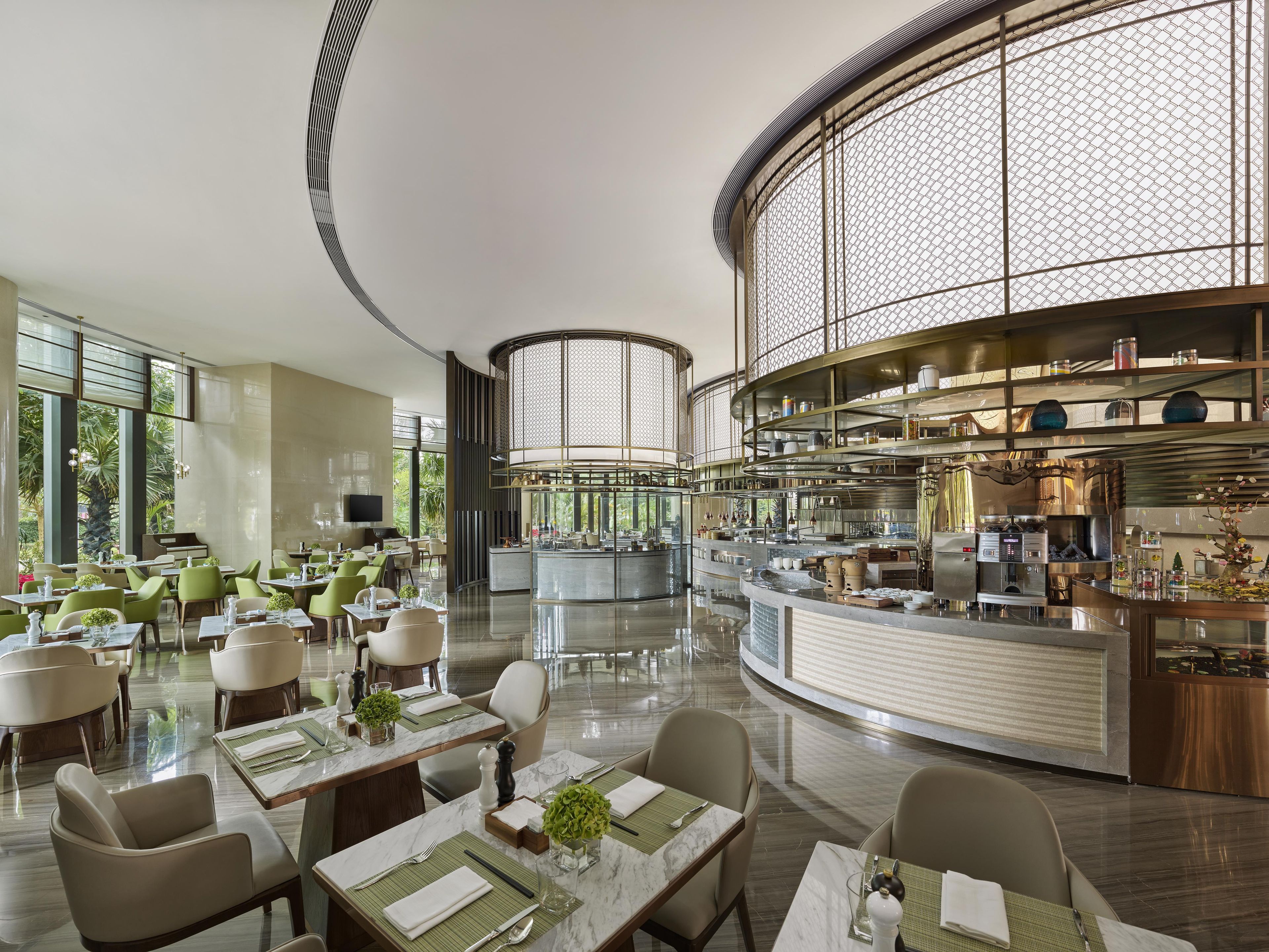 A modern restaurant with a central bar, dining tables with green placemats, and a piano in the background.