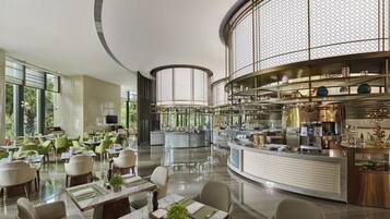 A modern restaurant with a central bar, dining tables with green placemats, and a piano in the background.