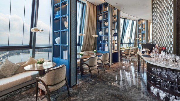 A modern interior with a bar area, seating, and large windows offering a city view. - Hilton Hainan Ocean Flower Island (Danzhou)