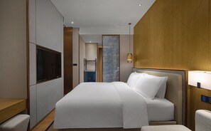A modern hotel room with a large bed, a TV, a desk, and a bathroom in the background. - Hilton Hainan Ocean Flower Island (Danzhou)