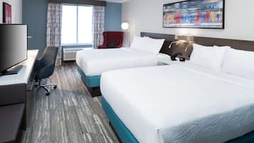Habitación de hotel con dos camas, un escritorio con televisor, una silla y un ventanal con cortinas.