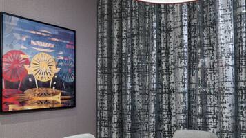 A room with a wooden coffee table, grey upholstered chairs, a red lamp, and a patterned curtain.
