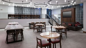 Een modern restaurant met ronde tafels, rechthoekige tafels en een trap naar een hoger niveau.