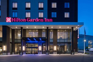 The exterior of a Hilton Garden Inn hotel with a modern facade, large windows, and a well-lit entrance.