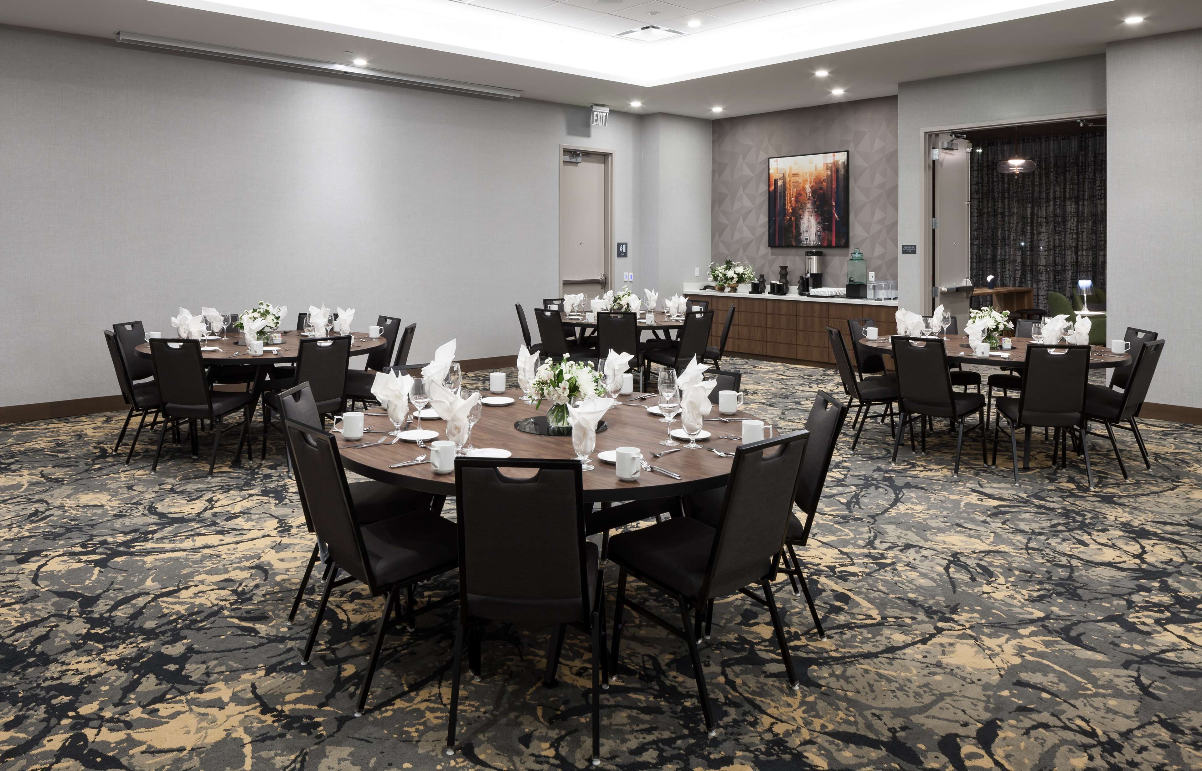 A conference room with round tables, black chairs, and a carpeted floor.