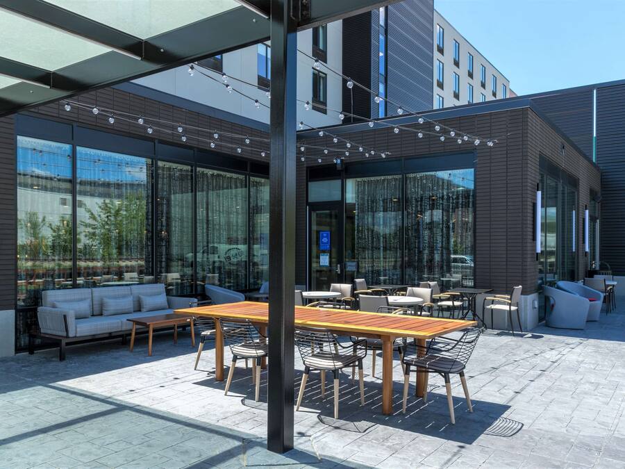 An outdoor seating area with a wooden table and chairs, a sofa, and a glass wall providing views of the surrounding area.