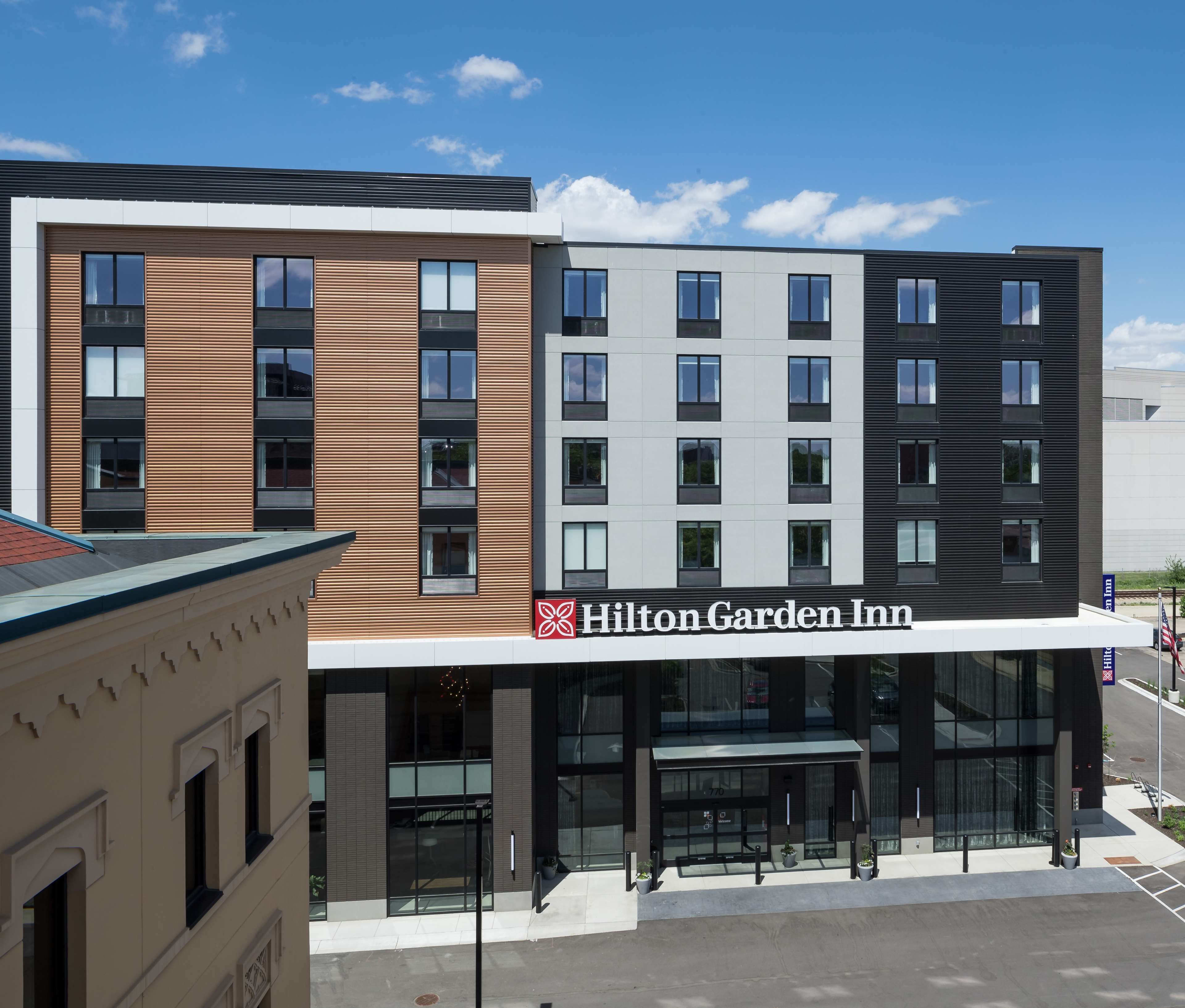 Een modern hotel met een opvallend Hilton Garden Inn bord, met een gevel van hout en metaal, grote ramen en een overdekte entree.