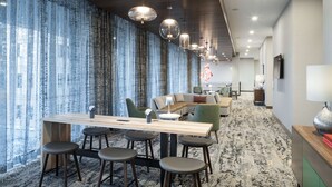 Een modern interieur met een lange houten tafel en barstoelen, een zithoek en een groot raam met gordijnen.