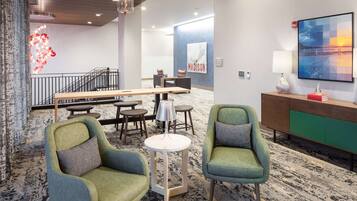 Un espace de détente moderne avec deux fauteuils verts, une table ronde, un coin bar et un grand tableau accroché au mur.