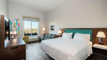 A hotel room with a large bed, a desk with a computer, a chair, a TV, and a window with a view of the desert.