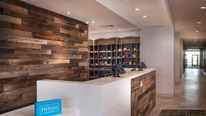 A hotel reception area with a wooden wall, marble reception desk, and shelves with various items. - Home2 Suites by Hilton Riverside March Air Force Base (March Air Reserve Base)