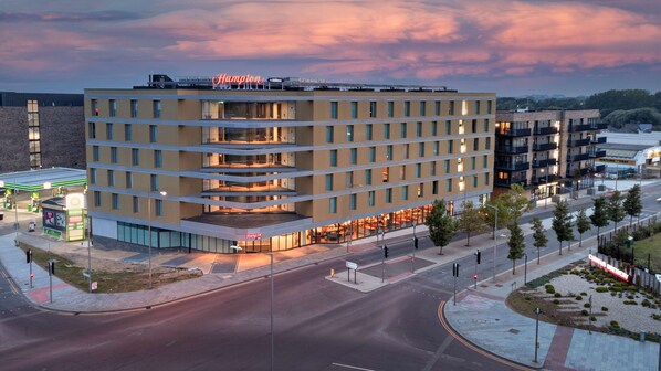 A multi-story hotel with a modern design, featuring a prominent entrance and a visible sign for Hampton.