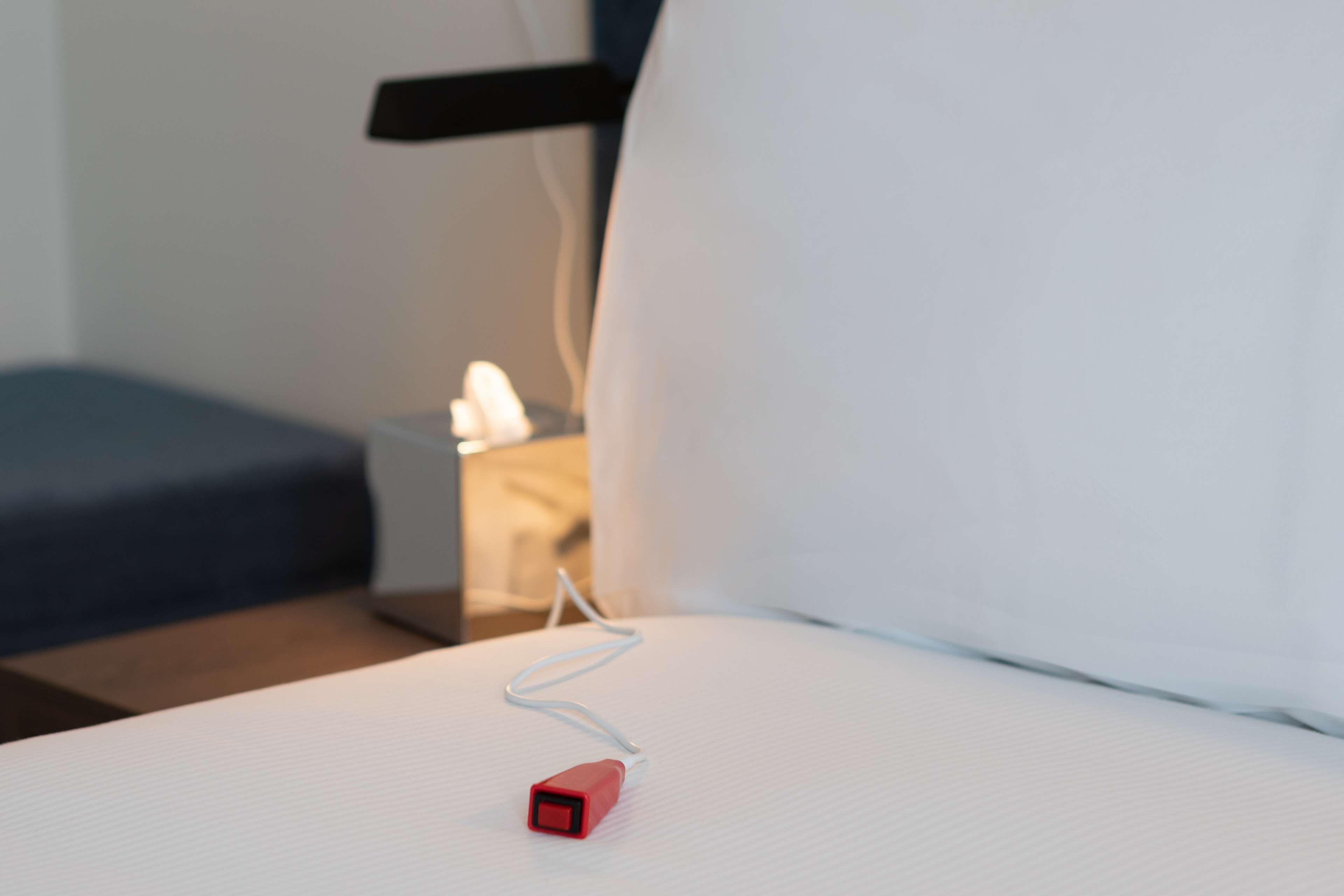 A bed with a white sheet and a red power adapter plugged in.