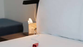 A bed with a white sheet and a red power adapter plugged in.