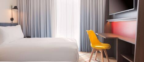 A hotel room with two beds, a desk with a chair, a TV, and a large window with curtains.
