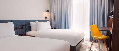 A hotel room with two beds, a desk, a chair, and a large window with curtains.