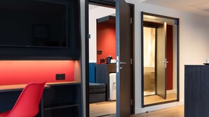 Een moderne hotelkamer met een bed, een bureau met stoel, een kledingkast en een deur naar een badkamer.