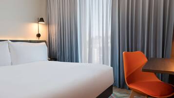 A hotel room with a bed, a chair, a table, and a lamp.