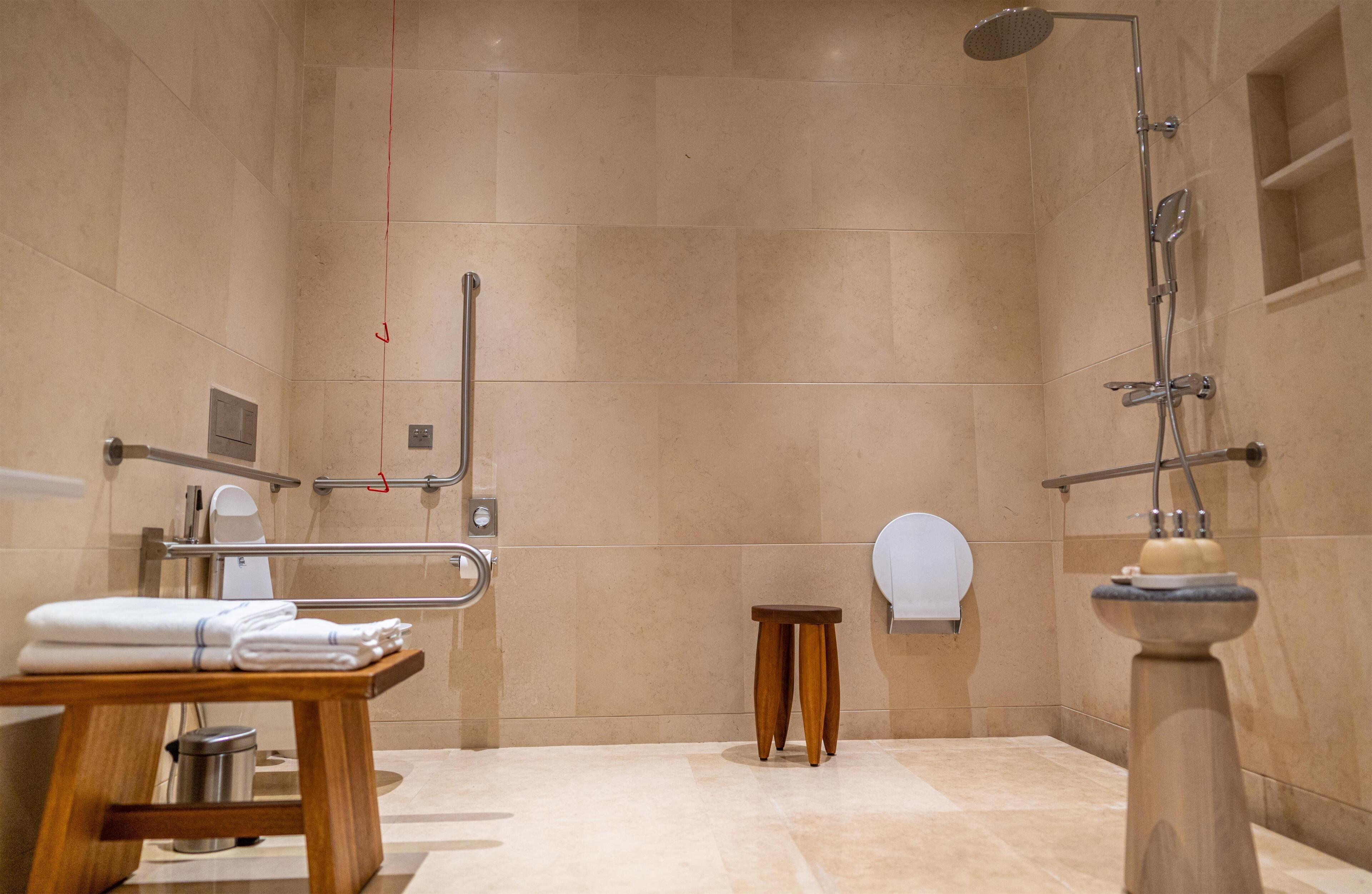 Un baño moderno con ducha, barras de apoyo, inodoro, lavabo y perchero para toallas.