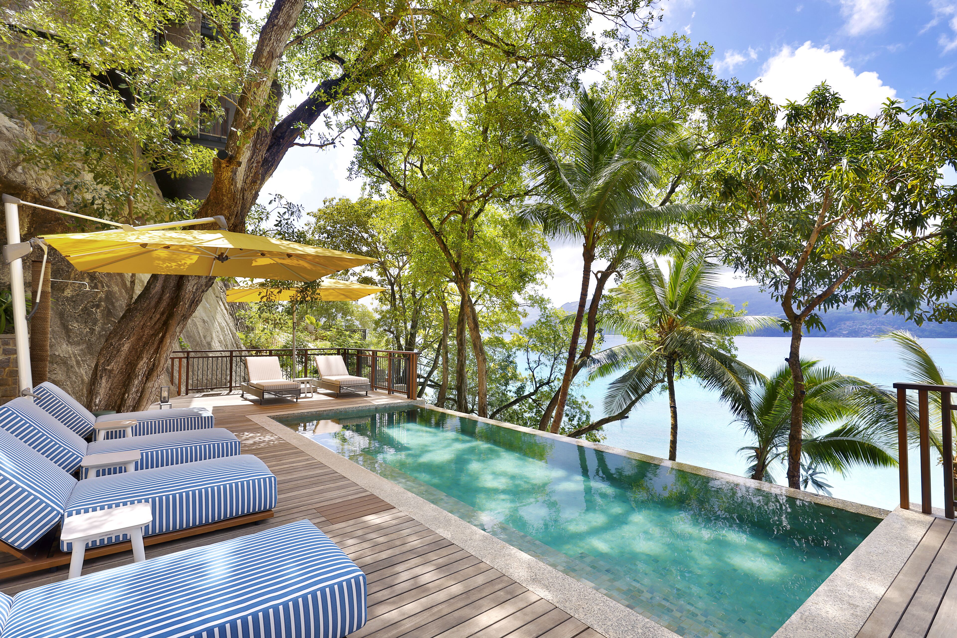 An infinity pool with lounge chairs and umbrellas, surrounded by palm trees and a view of the ocean.