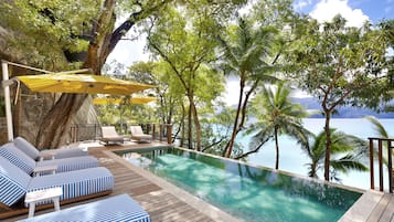 An infinity pool with lounge chairs and umbrellas, surrounded by palm trees and a view of the ocean.