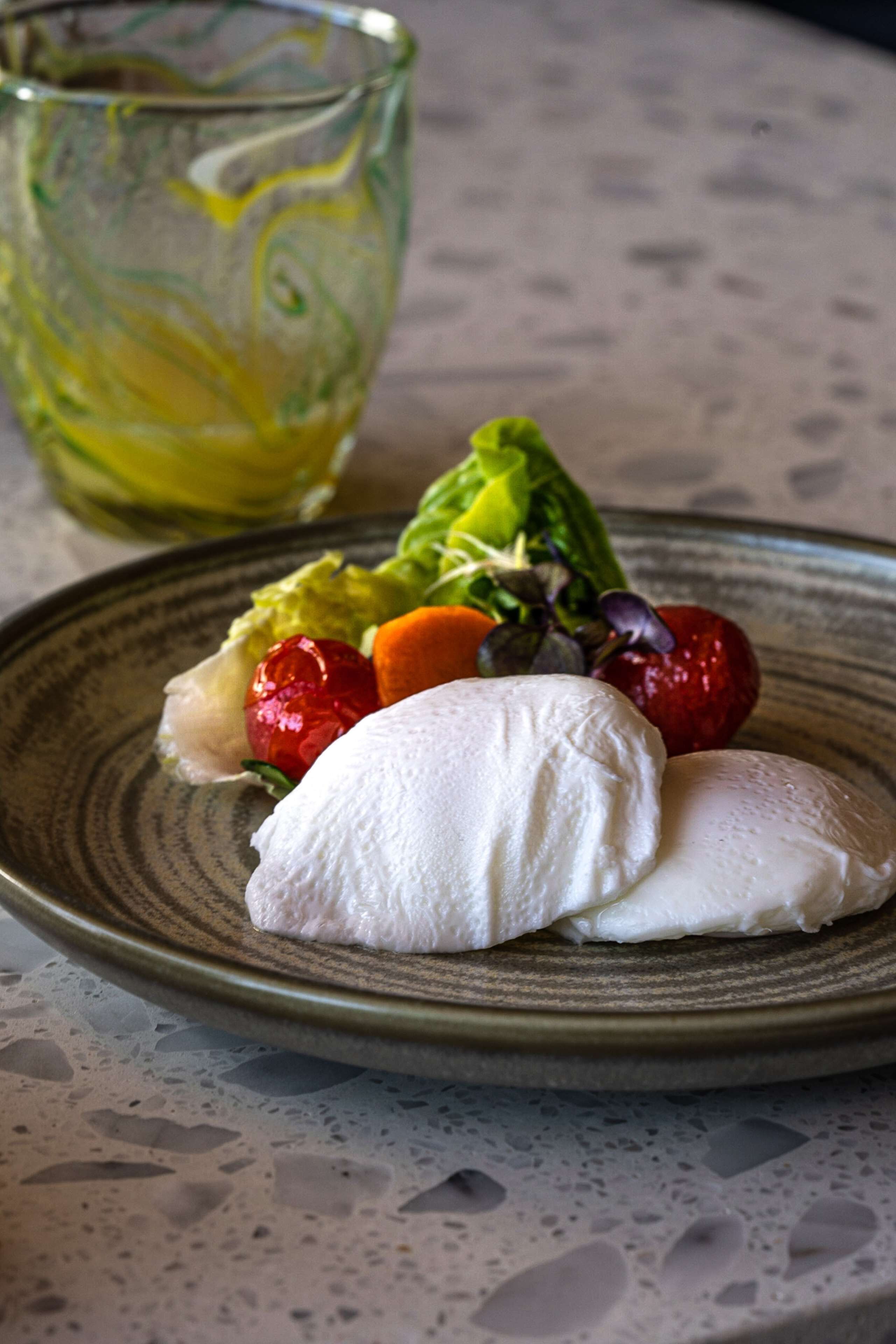 A plate with a dessert consisting of a scoop of ice cream and fresh fruit, accompanied by a glass of a yellow beverage.