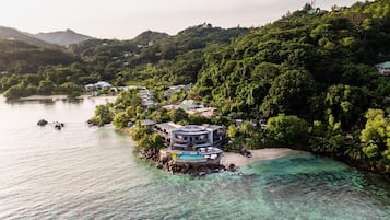 An aerial view of a coastal resort with villas, a swimming pool, and lush greenery.