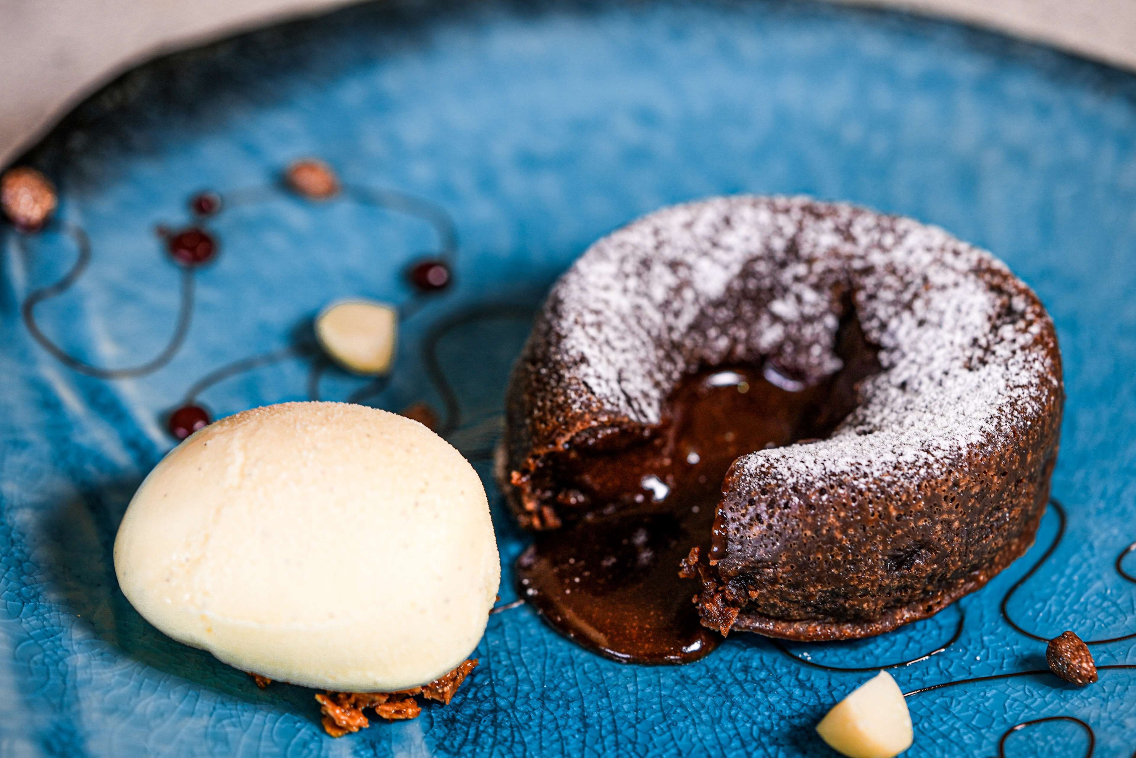 A dessert consisting of a chocolate lava cake and a scoop of vanilla ice cream on a blue textured plate.