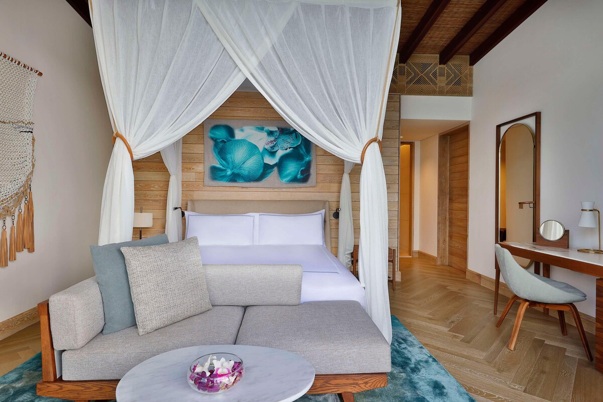A bedroom with a bed, a sofa, a desk, and a mirror.