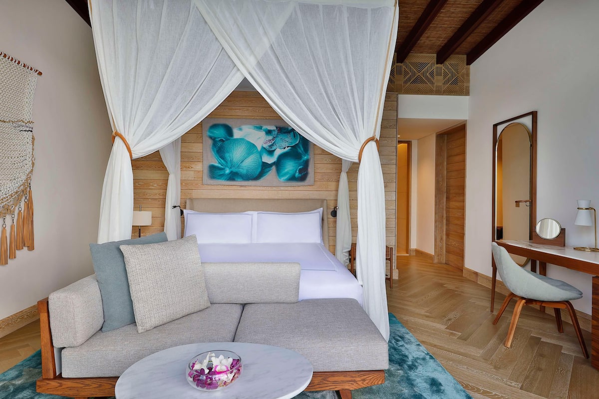 A bedroom with a bed, a sofa, a desk, and a mirror.